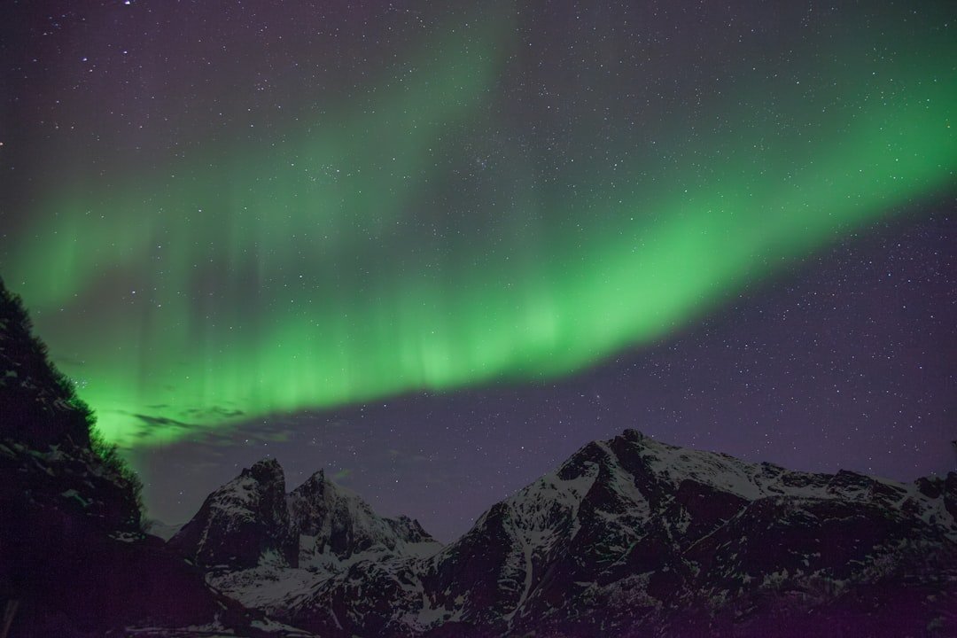 Vibrant green northern lights dancing over a snowy mountain landscape with a photographer silhouette in foreground